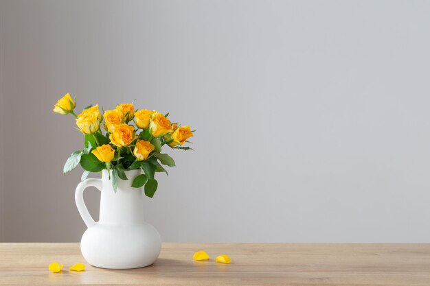 roses jaunes dans une cruche blanche sur une étagère en bois