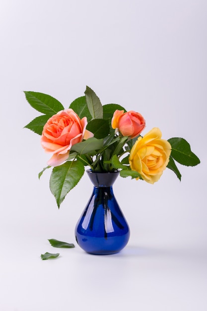 Roses jaunes et pêches fraîches dans un vase bleu isolé sur une surface blanche