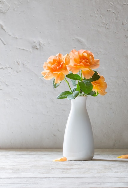 Roses orange dans un vase sur un mur blanc de surface