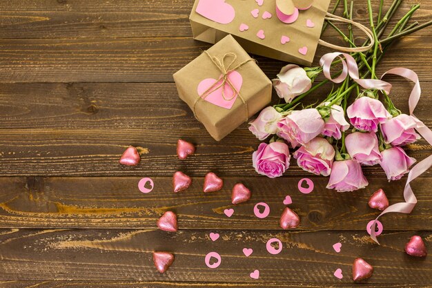 Roses roses et cadeaux emballés dans du papier recyclé sur une table en bois rustique.