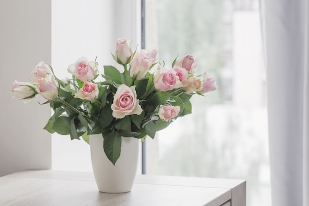 Roses roses dans un vase sur la fenêtre