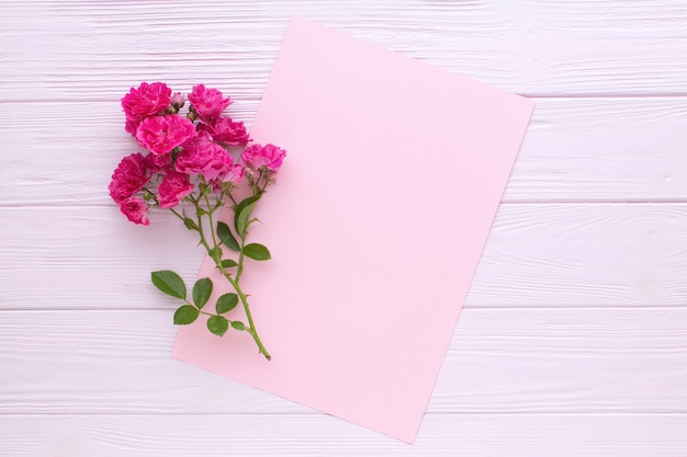 Roses roses et feuille de papier rose vierge sur table en bois