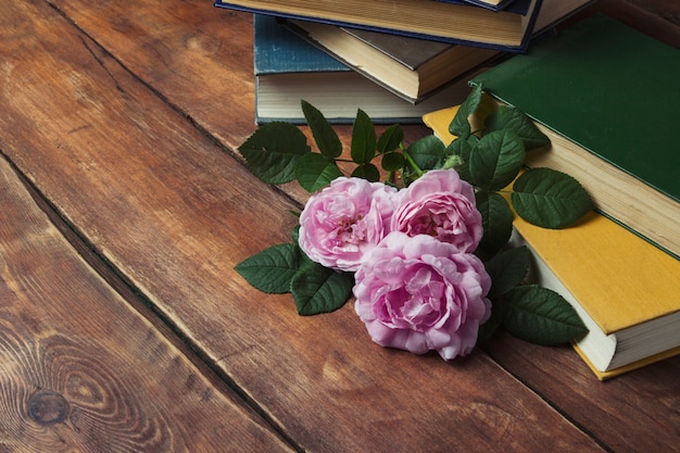 Roses roses et livre avec une couverture jaune sur un fond en bois. Le concept d'histoires romantiques et de romans