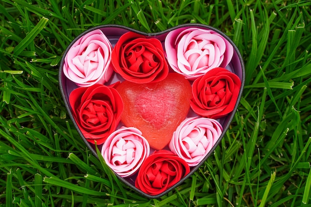 Roses roses et rouges vives faites de copeaux de savon avec des coeurs sur l'herbe verte dans une boîte en forme de coeur vale...