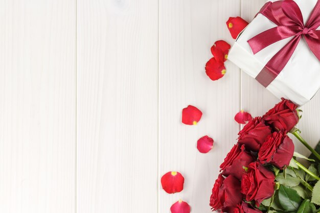 Roses rouges et boîte-cadeau sur une table en bois blanche, vue de dessus