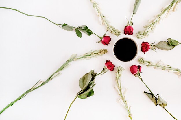 Roses rouges et cadre de fleurs blanches avec tasse de café sur une surface blanche