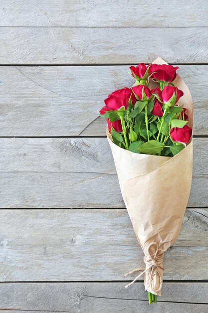 Roses rouges enveloppées dans du papier sur fond de table en bois