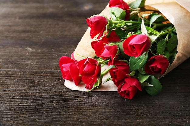 Photo roses rouges enveloppées dans du papier sur fond de table en bois