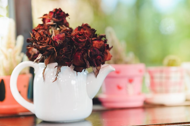 Photo des roses rouges foncées séchées dans un vase blanc sur une table en bois dans une maison