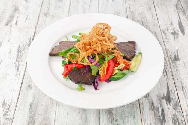 Rôti de boeuf au paprika rôti et légumes. Dans une assiette blanche. Fond en bois clair. Vue d'en-haut.