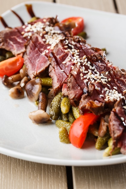 Rôti de boeuf mi-saignant aux cornichons, tomates cerises, champignons sur une plaque blanche