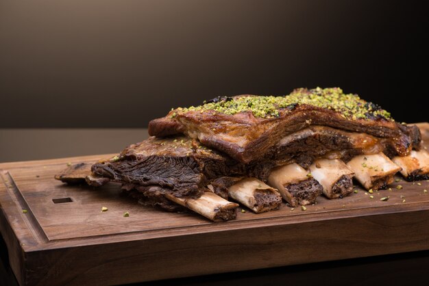 Rôti de viande avec os sur un plateau en bois, fond sombre, isolé