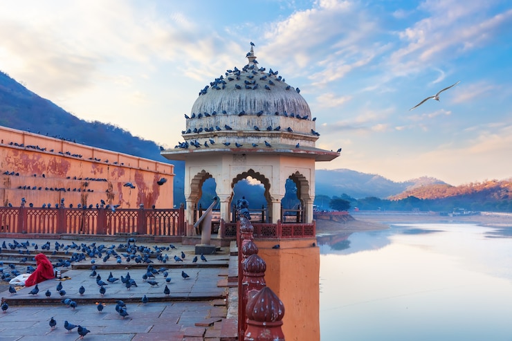 Photo rotonde d'amber fort, dame indienne nourrir les pigeons par le lac maotha, jaipur, inde.