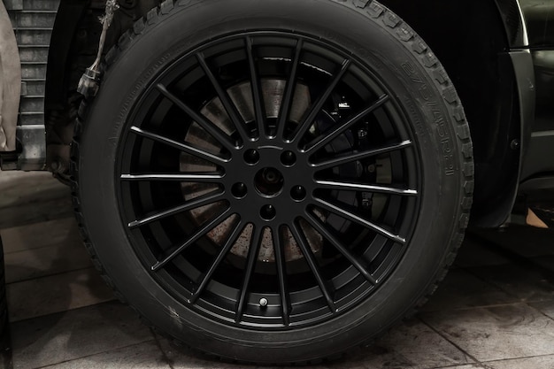 Une roue en alliage d'aluminium avec des pneus cloutés d'hiver sur une voiture noire avec un nouveau disque de frein nécessitant un remplacement Météo et transport Industrie des services automobiles
