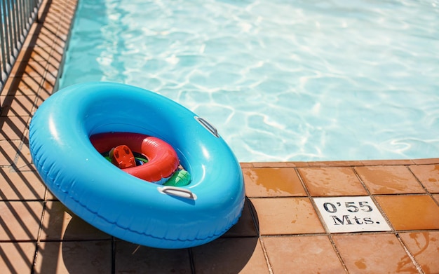 Roue gonflable bleu vif et jouets aquatiques à côté de la piscine éclairée par le soleil
