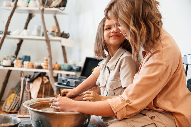 Photo roue de poterie mère avec petite fille faisant des pots de céramique dans l'atelier