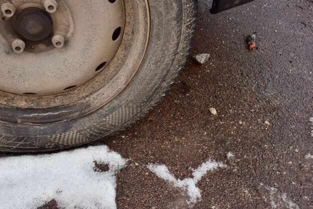 Roue sale d'une voiture de tourisme sur le plan rapproché d'asphalte couvert de neige