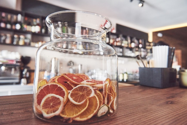 Roues Séchées D’orange Confite, Citron Vert Et Citron Dans Un Grand Récipient En Verre, Le Contenu étant également Rangé Dans Un Bloc De Boucher Autour D’un Pot Avec Du Sucre Brut Et Un Couvercle En Métal