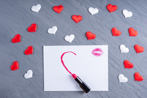 Rouge à lèvres dessine une forme de demi-coeur sur du papier blanc avec des bisous de rouge à lèvres sur un fond en bois gris