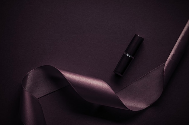 Rouge à lèvres de luxe et ruban de soie sur fond de vacances violet foncé maquillage et cosmétiques flatlay pour la conception de produits de marque de beauté