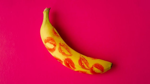 Rouge à lèvres rouge sur une banane jaune sur fond rose. Concept d'amour et de sexe.