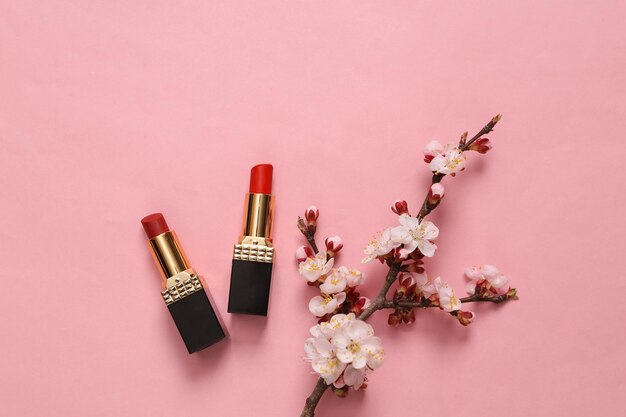 Rouge à lèvres rouge et belles branches fleuries sur fond rose Concept de beauté de printemps Mise à plat Vue de dessus