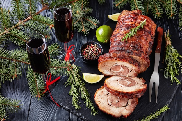 Roulade de porc rôti en tranches - Porchetta, délicieux rôti de porc de la tradition culinaire italienne de vacances sur un plateau en ardoise avec sapin et vin rouge, close-up, recette authentique