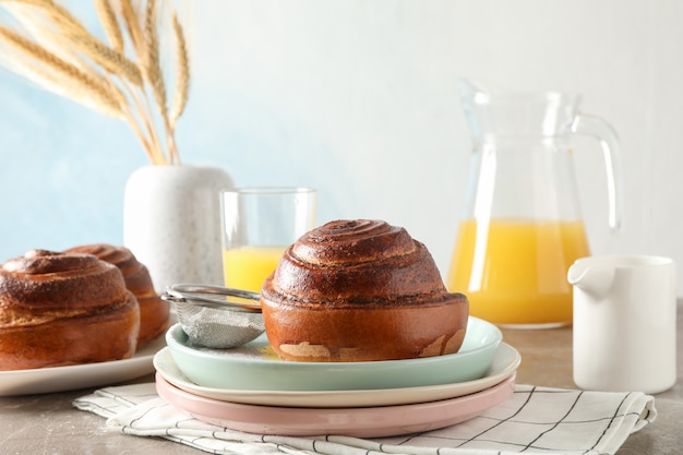 Rouleau de cannelle fraîchement cuit sur une plaque de couleur avec du jus d'orange sur une table brune.