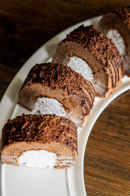 Un rouleau de chocolat avec de la crème fraîche sur une assiette blanche et un fond en bois