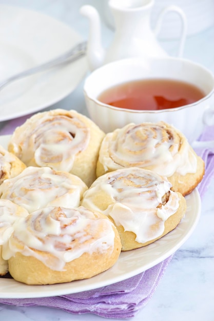 Photo rouleau de cinnabon fait maison avec de la crème sur une assiette blanche et une tasse de thé fond clair mise au point sélective sur le petit pain petite profondeur