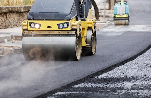 Rouleau compresseur et finisseur d'asphalte sur le chantier, avec béton chaud et fumée