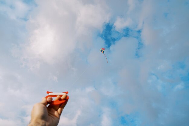 Photo un rouleau de fil avec un cerf-volant volant dans un ciel nuageux dans la main d'un homme
