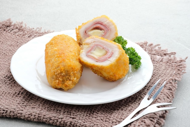 Rouleau de filet de poulet bleu Cordon croustillant avec jambon et fromage Servi dans une assiette sur fond gris