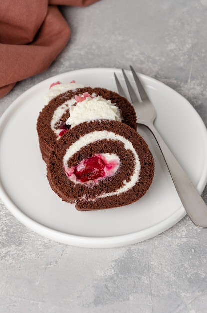 Rouleau de gâteau au chocolat forêt noire avec crème fouettée et garniture aux cerises sur fond gris. Copiez l'espace.