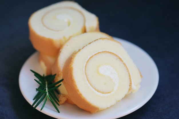 Rouleau de gâteau éponge tranches bonbons dessert rouleau de crème collations à la vanille et concept alimentaire Swiss Roll Cake Gâteau rouleau sur plaque gâteau au romarin sur table