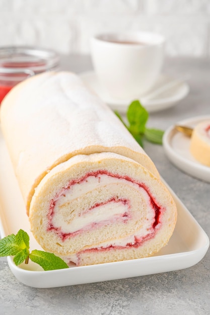 Rouleau de génoise avec confiture de fraises et crème sur une plaque blanche sur fond gris Espace de copie