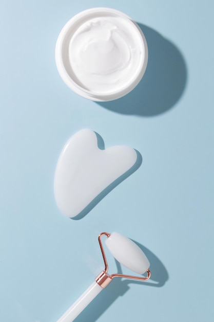 Rouleau de jade blanc et outil gua sha sur fond bleu pastel Outil de beauté tendance Composition minimale