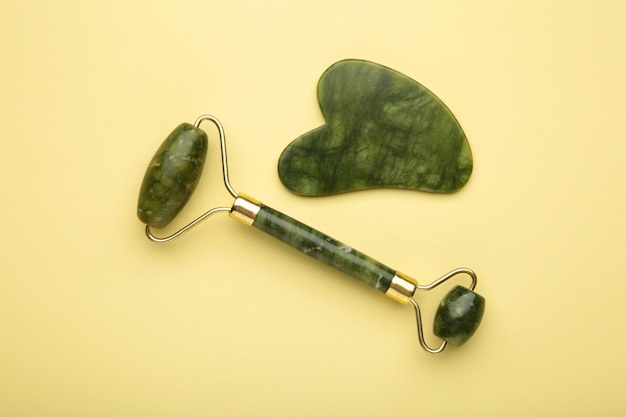 Rouleau de jade vert et pierre de gua sha pour le massage du visage et sur fond beige Accessoires de beauté et d'autosoins pour la maison Rouleau pour le visage pour le traitement anti-rides Vue de dessus à plat