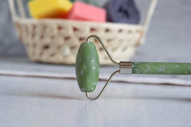 Rouleau de jade vert pour le massage facial et une branche verte sur fond de marbre