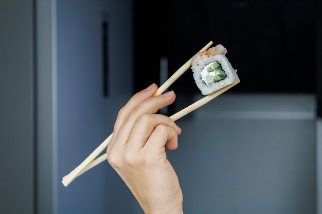 Rouleau japonais Philadelphie La fille tient des sushis avec des baguettes Arrière-plan flou