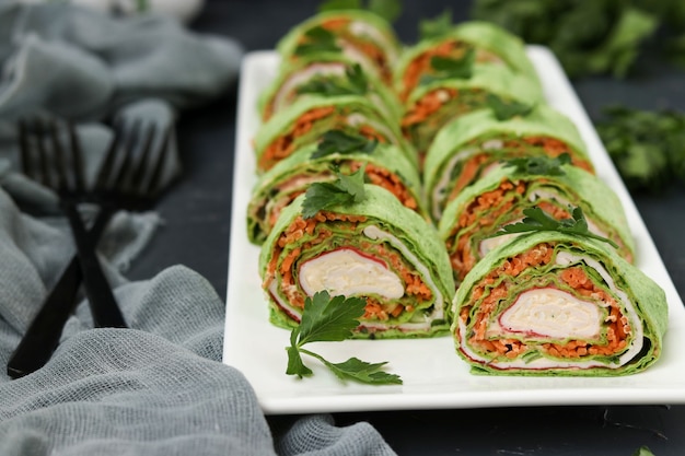 Photo rouleau de lavash avec bâtonnets de crabe, épinards, persil, fromage et carottes dans un style coréen sur une assiette sur un fond sombre