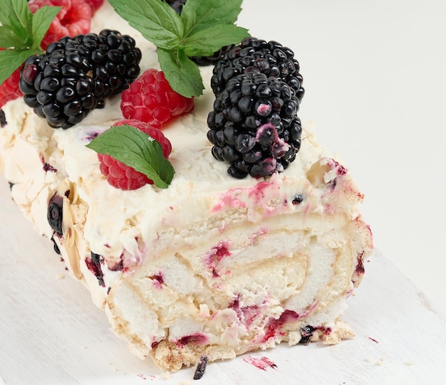 Rouleau de meringue au four avec de la crème et des fruits frais sur une planche en bois blanc délicieux dessert