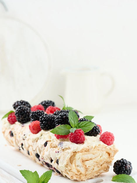 Rouleau de meringue au four avec de la crème et des fruits frais sur une planche en bois blanc délicieux dessert