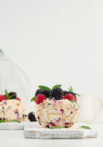 Rouleau de meringue cuit au four avec de la crème et des fruits frais sur une planche de bois blanc