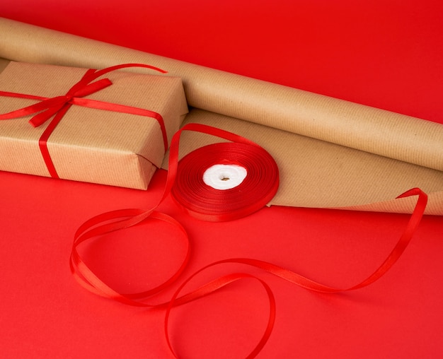 Rouleau de papier brun pour l'emballage, une bobine de ruban rouge un cadeau emballé en papier kraft brun sur rouge