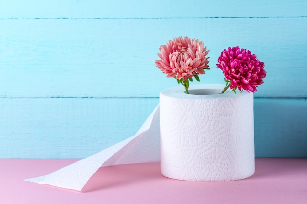 Rouleau de papier toilette parfumé et fleurs sur une table rose. Papier toilette avec une odeur. Concept d'hygiène. Concept de papier toilette