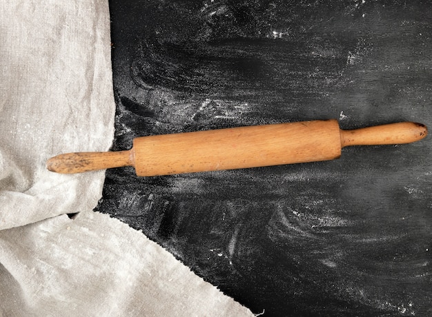 Rouleau à pâtisserie en bois sur fond noir, farine de blé blanche