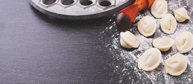 Rouleau à pâtisserie, boulettes crues dans la farine sur un fond noir.