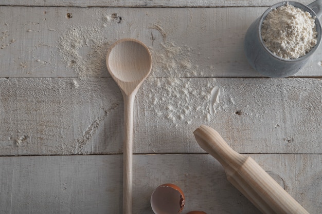 Rouleau à pâtisserie et cuillère en bois pour faire de la pâte sur fond de bois blanc.