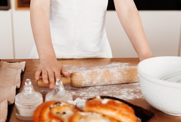 rouleau à pâtisserie pour la pâte dans les mains des enfants sur la table dans la cuisine